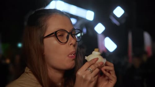 Ein Mädchen mit Brille hält Mochi in den Händen und nimmt einen großen Bissen, während es süße Leckerbissen inmitten von lebhaften Speisen genießt