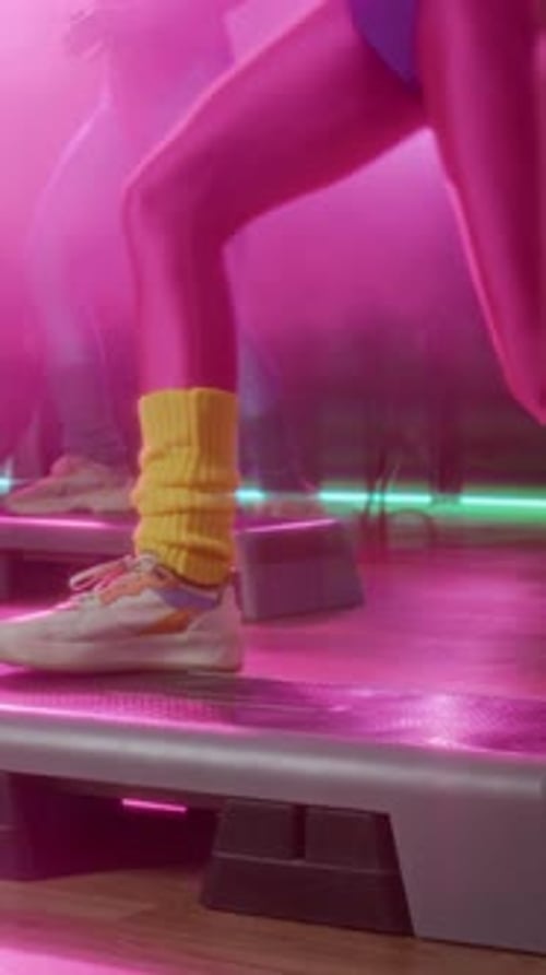 Women Perform Step Aerobics in Studio with Pink Lighting