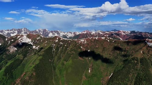 Lush Green Mountain Slopes and Snowy Peaks Under Dramatic Clouds