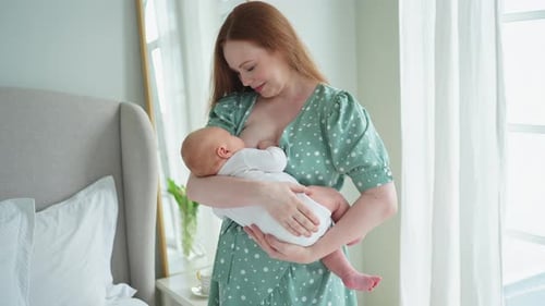Woman Breastfeeding Baby in Bright Bedroom