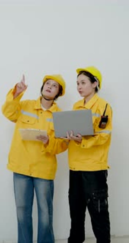 Asian female engineer and woman architect review laptop, blueprint, pointing upward during