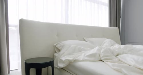 Unmade Bed with Upholstered Headboard and Bedding Linen in Modern Bedroom