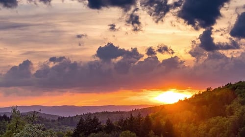 Mehrfarbiger Sonnenuntergang am bewölkten Himmel über einem Gebirgstal mit einem Herbstwald