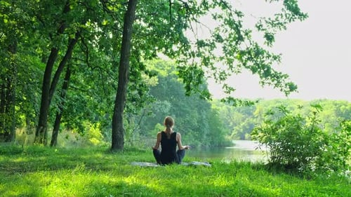 Woman Meditating by Calm Lake on a Sunny Day