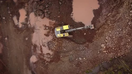 Yellow excavator removing rocky soil in open stone quarry, Brazil. Aerial top-down descending direct