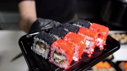 A Closeup Chef in Gloves Holds a Plate of Sushi in the Restaurant's Kitchen