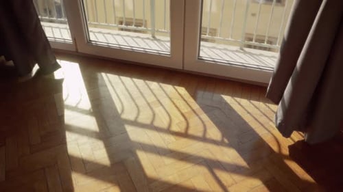 Sonnenlicht fällt durch das Fenster ein und erzeugt Schatten auf dem Holzboden in der Wohnung. Helles Tageslicht in