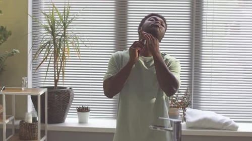 Man Shaves Beard with Electric Razor in Bathroom