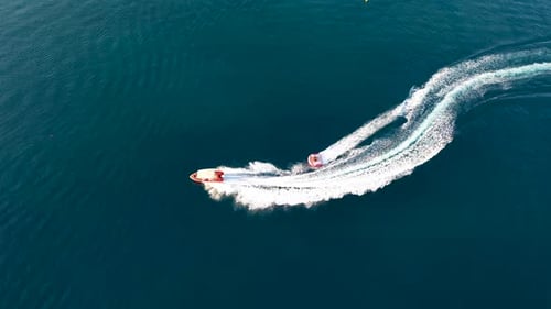 Top down view of speed boat towing a ski. The ski or wakeboard crosses over the boat's wash against