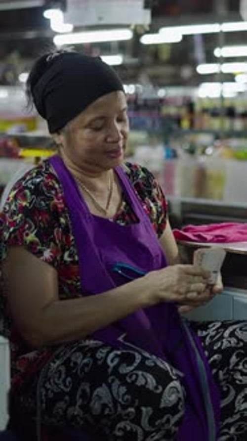 Mulher asiática madura sentada ao lado de sua barraca de mercado de peixe contando as notas que ela tem em suas mãos