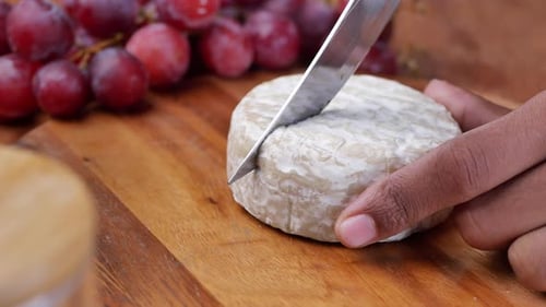 Cutting Camembert Cheese on a Chopping Board on Table