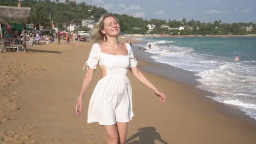Young Happy Woman Walking Along a Tropical Sea Beach in a Summer Dress