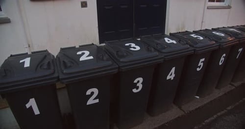 Numbered rubbish bins awaiting collection along street curb, pan