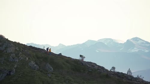 Two persons walking down a steep hill, surrounded by mist and mountains.