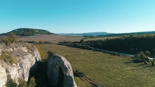Rocky Cliff Overlooking Green Valley with Clear Blue Sky