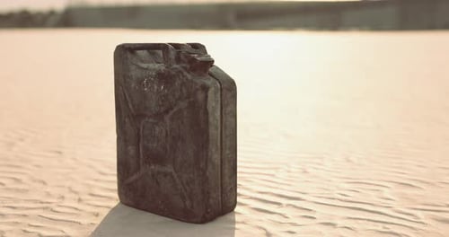 Black Metal Canister Placed on Sunlit Sandy Ground in a Desert Setting