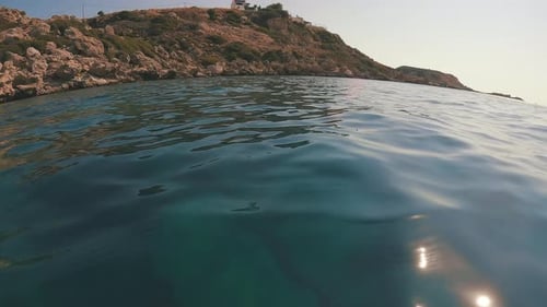 Camera moving forwards low above water to rocky shore