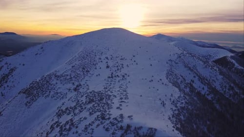 Flying over snowy mountain peaks at sunset