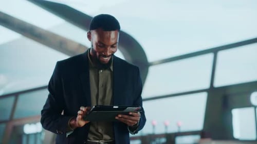 A businessman in a suit uses a tablet in an airport terminal.