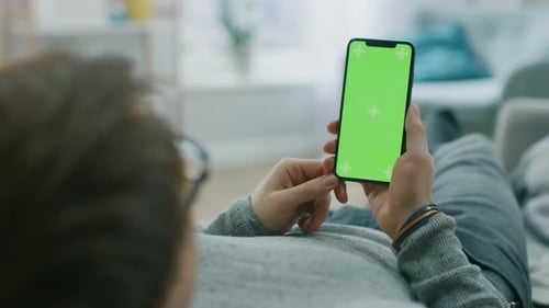 Man at Home Lying on a Couch using Smartphone with Green Mock-up Screen, Doing Swiping, Scrolling G