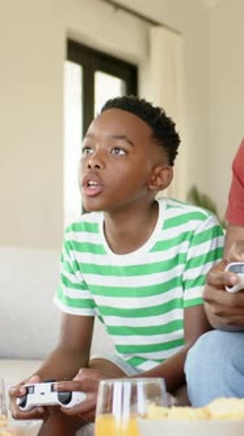 Vertikales Video: Spielender Junge im gestreiften Tee, der zu Hause beim Spielstart den Controller drückt, um die Eltern zu schlagen