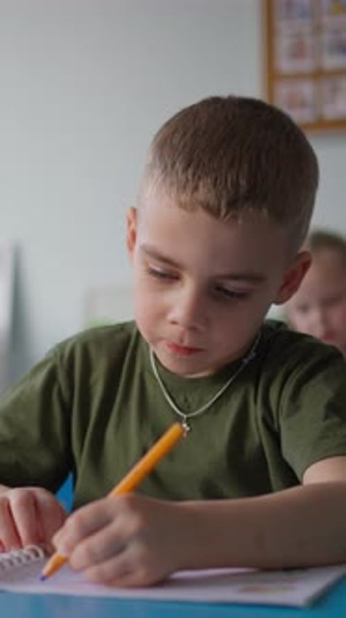 Young Boy with Short Hair Concentrating Intently As He Writes with a Pencil on Paper While in a
