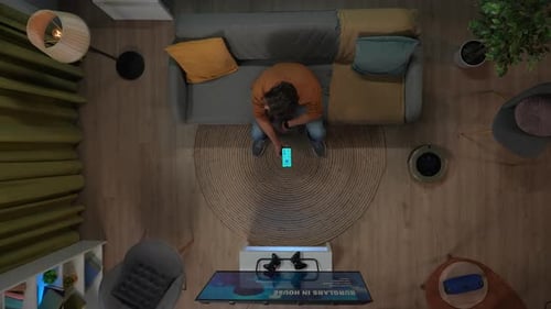 Top View of Man Sitting on the Couch in the Room and Switching on House Gadgets Using App on