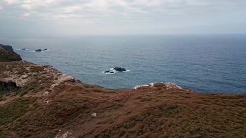 Drone Rocky Coastal Shoreline with Steep Stone Cliffs Meeting Ocean Waves