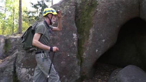 A Mature Male Adventurer with Hiking Equipment Exploring a Forest Cave