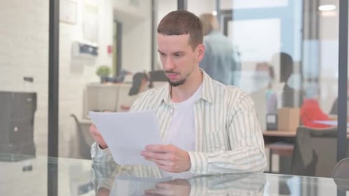 Young Adult Reviews Documents in a Modern Office