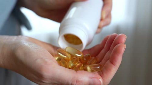 Hand Pours Vitamin Capsules into Palm of Hand