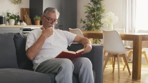 Senior Man Relaxing and Reading Book on Couch