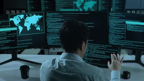 Asiatischer Mann arbeitet mit Tablet, während er Code mit mehreren Computerbildschirmen im Büro schreibt