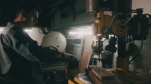 A worker works on a metal drilling machine in a workshop