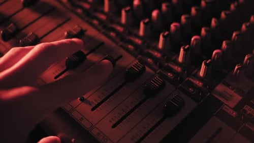 Sound Engineer Hand Adjusting Mixer Faders in Dark Studio