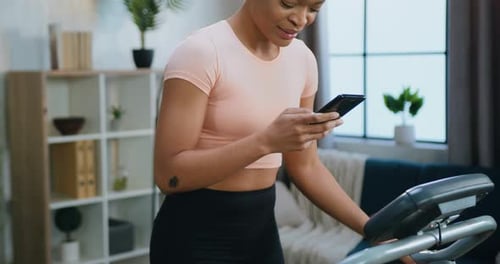 Woman Using Smartphone on Treadmill at Home