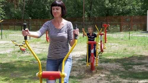 Mom and Son on Street Exercise Machines Go in for Sports in Slow Motion