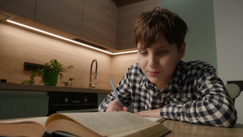 Teenager Studying Book and Writing in Kitchen