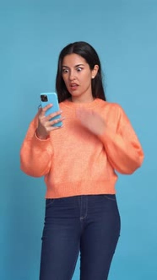 Shocked Woman Looking at Phone on Blue Background