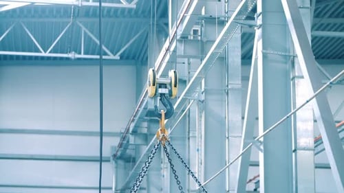 Industrial crane lifting heavy load with strong chains at manufacturing plant