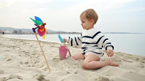 Cute little baby boy digging sand on the sea beach with a shovel