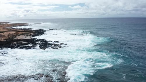 Waves crashing on volcanic shoreline with turquoise surf – aerial view