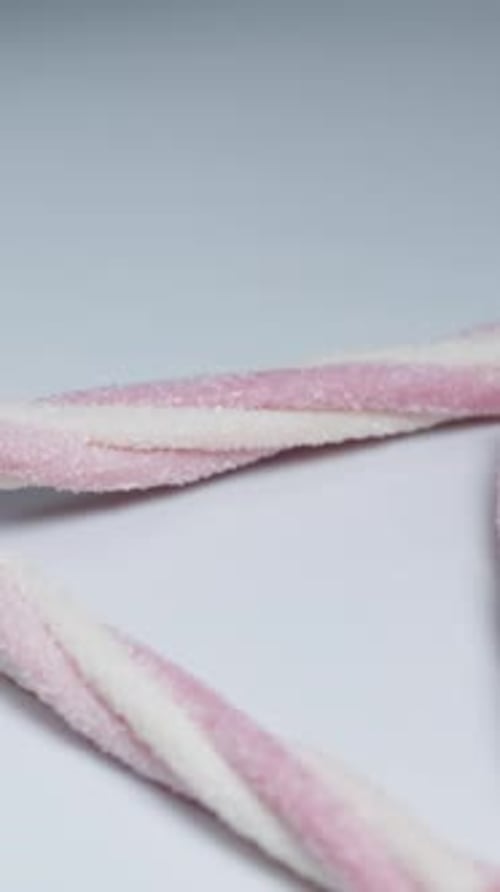 Pink twisted gummy sticks with sugar fall onto the table.