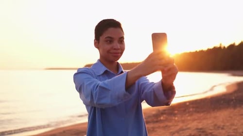 Young Woman Taking Photo on Beach at Sunset