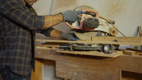 Close up hands of carpenter cutting wood with saw in construction site.