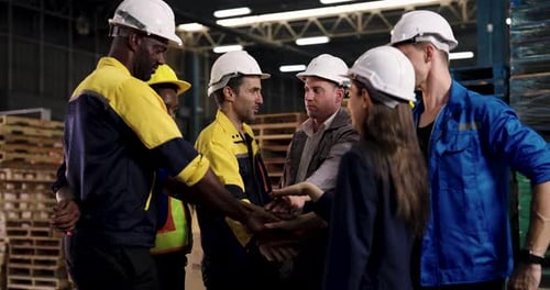 multiracial warehouse workers stacking hands in slowmotion teamwork gesture to build trust and