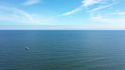 calm aerial footage over the ocean on a warm afternoon. a small boat is visible and then a bird spe