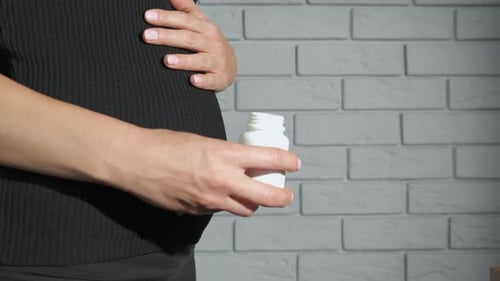 Pregnant Woman Pouring Pills into Hand Indoors