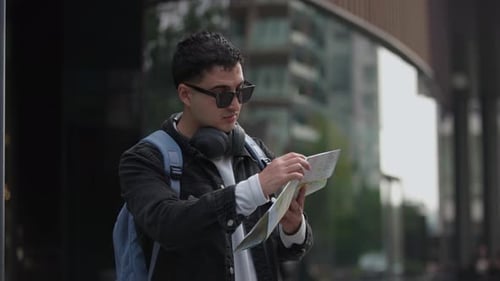 Latin Male Traveler Stopping to Check Map in Front of Modern Urban Building