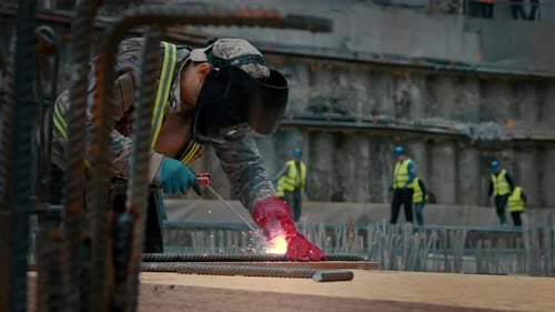 A worker at a construction site welds metal with a welding machine